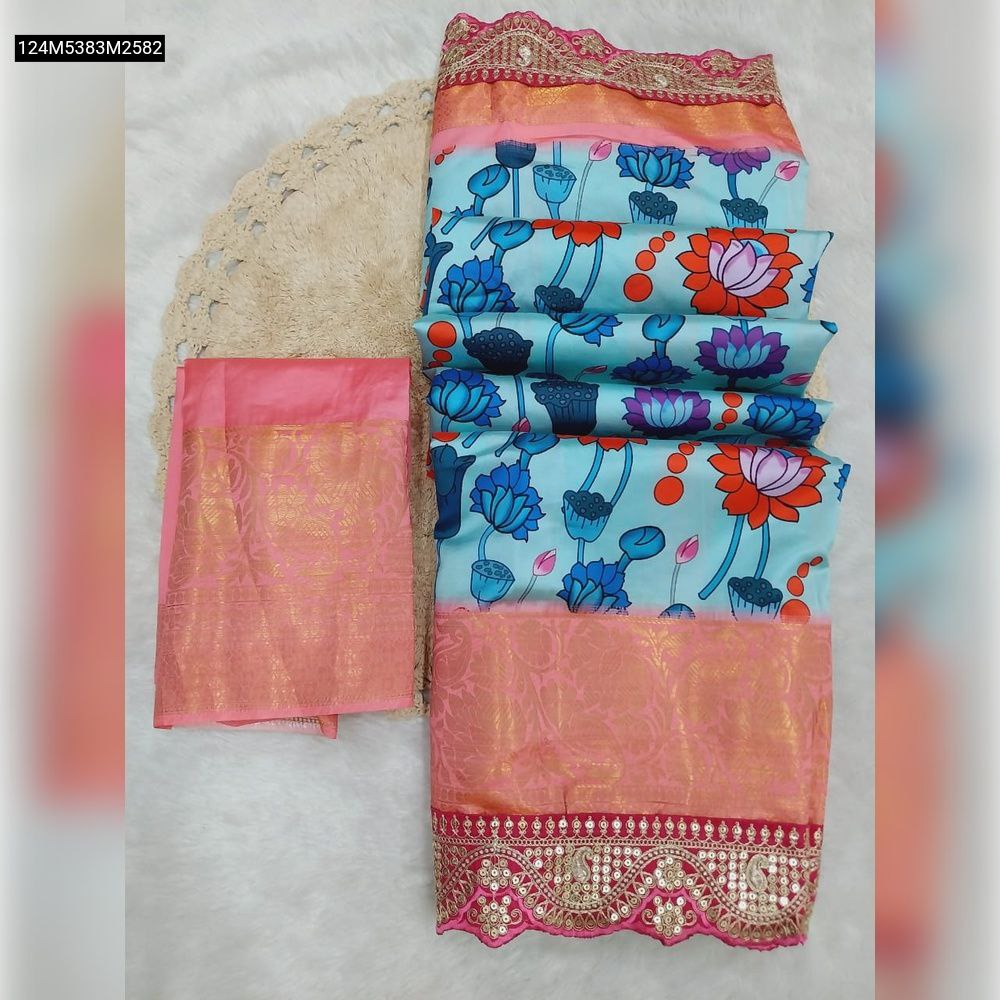 Top-down view of a folded TRENDBUY Light Blue Dola Silk Saree with multi-color lotus prints, a pink jacquard border, and a pink contrast blouse on a white fluffy surface.