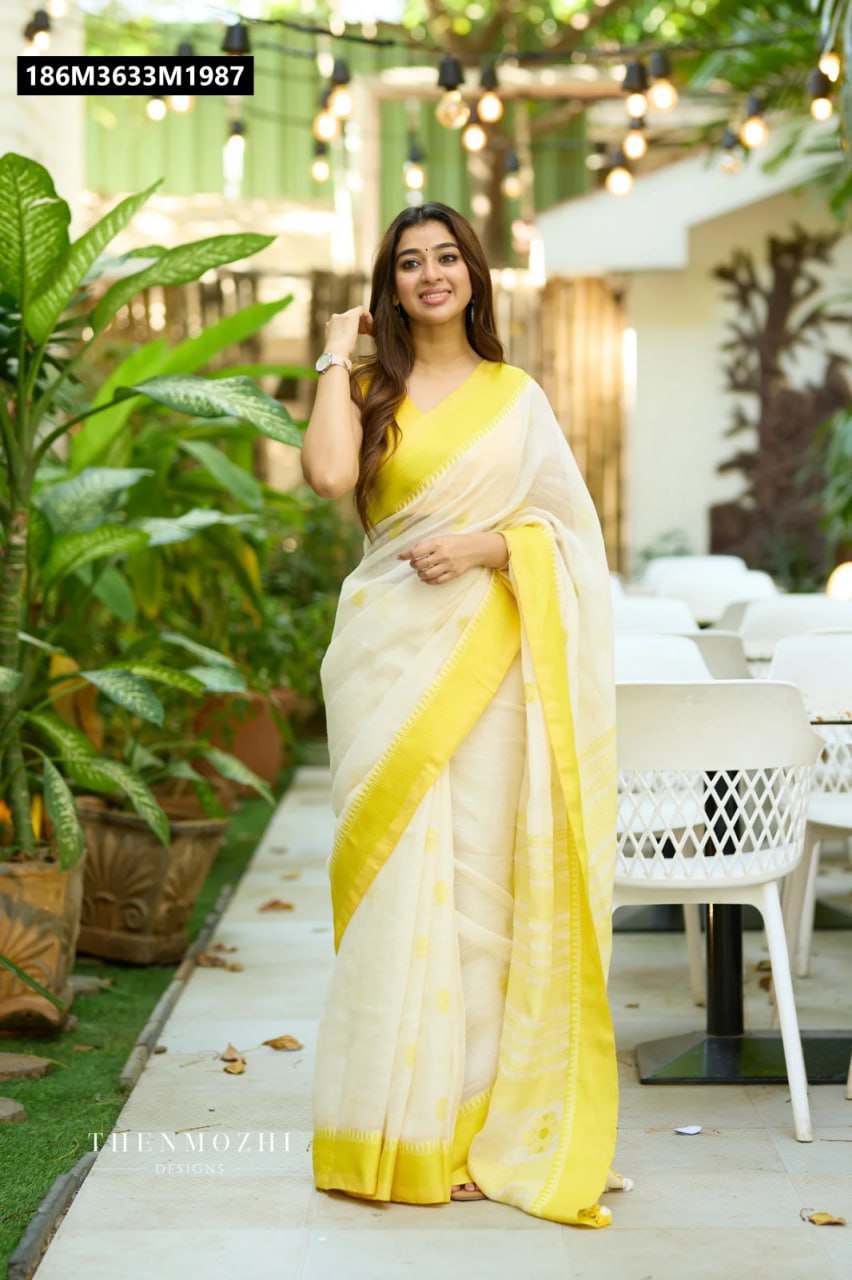 Model showcasing TRENDBUY Soft Lilan Saree in cream with a vibrant yellow border and blouse, smiling outdoors in a cafe-like setting.