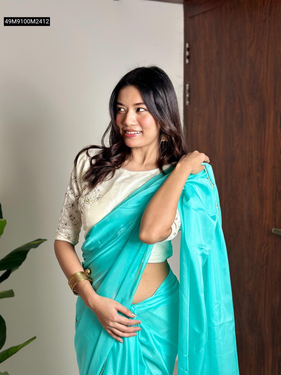 Smiling model draped in a radiant aqua blue organza saree, showcasing a side profile view of the saree and embroidered off-white blouse.