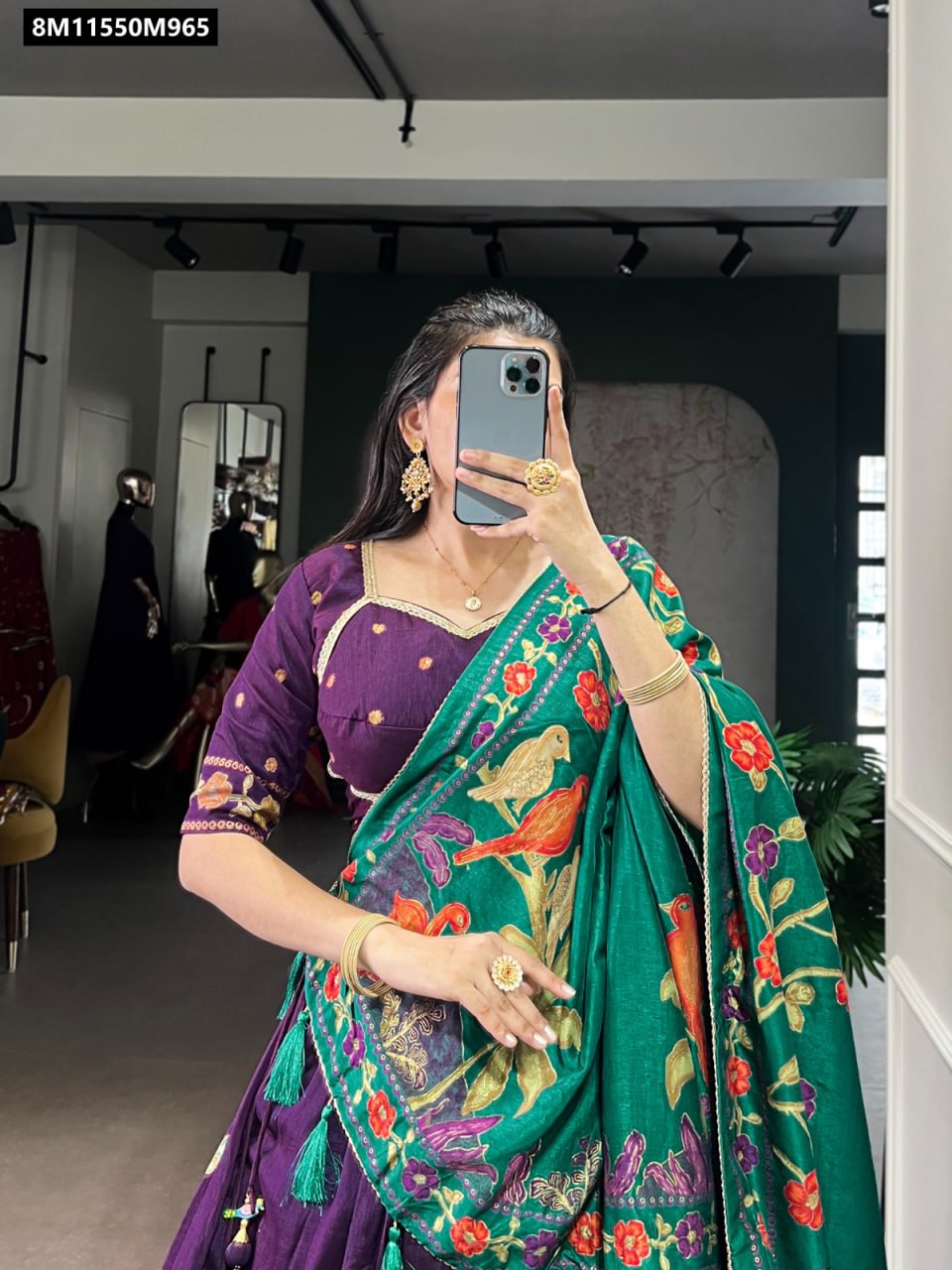 Close-up of a woman in a purple Tasar Silk lehenga choli with a green dupatta, showcasing intricate foil and floral print, posing indoors and holding a phone.