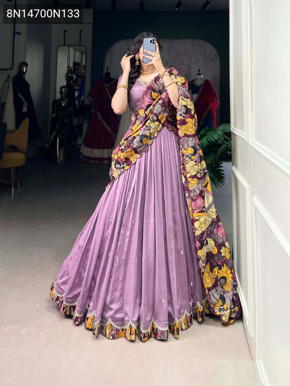 Full-body shot of a model wearing a lavender Vichitra silk lehenga choli with intricate sequins and thread embroidery, paired with a vibrant Kalamkari print tasar silk dupatta, taken in a fitting room.