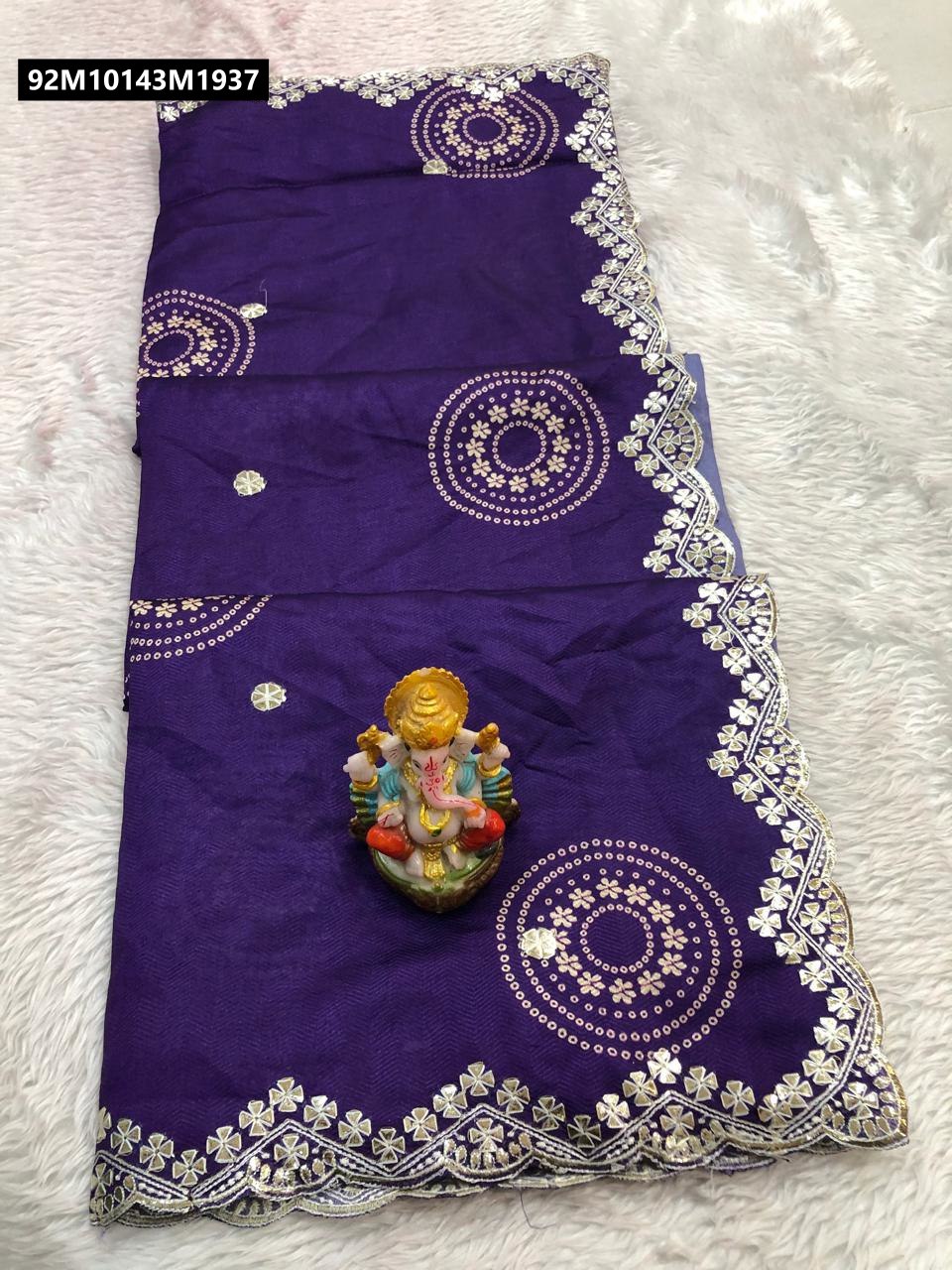 Folded purple Doria cotton saree with intricate Gotapati border and circular motifs, displayed on a fluffy white surface with a small Ganesha idol.