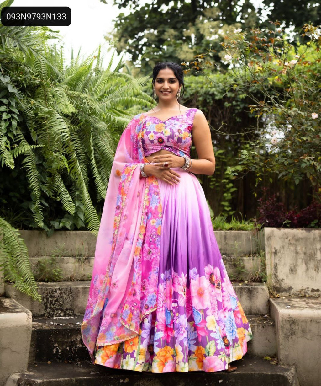 TRENDBUY model in full shot, smiling, standing on outdoor steps, wearing a vibrant purple-to-pink ombre floral printed Chinon lehenga choli with a matching dupatta.