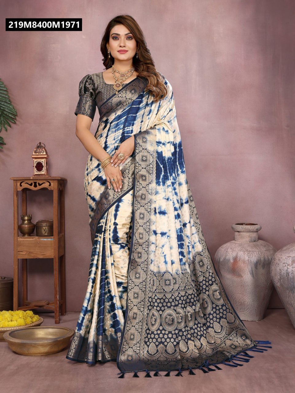Full body shot of a model elegantly draped in a blue and cream Shibori satin silk saree with heavy zari border, standing in a traditional setting.