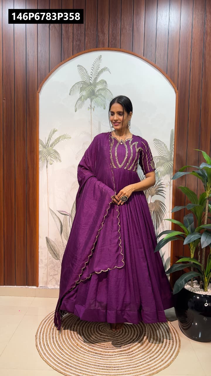 Model wearing a plum purple Vichitra silk Anarkali gown with sequin work, posing gracefully against a patterned wall.