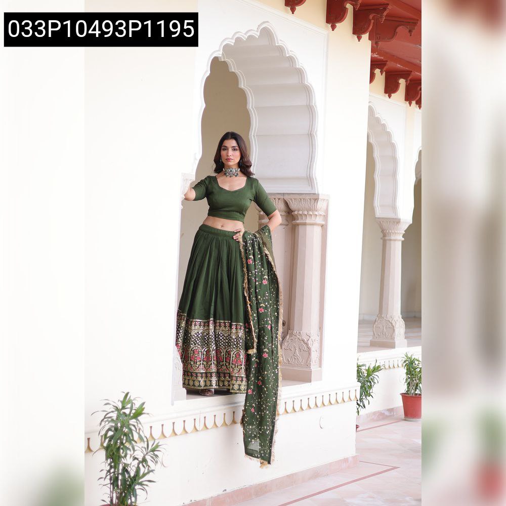 Full body shot of a model in an olive green Vichitra silk lehenga choli set with intricate embroidery, standing gracefully on a white archway.