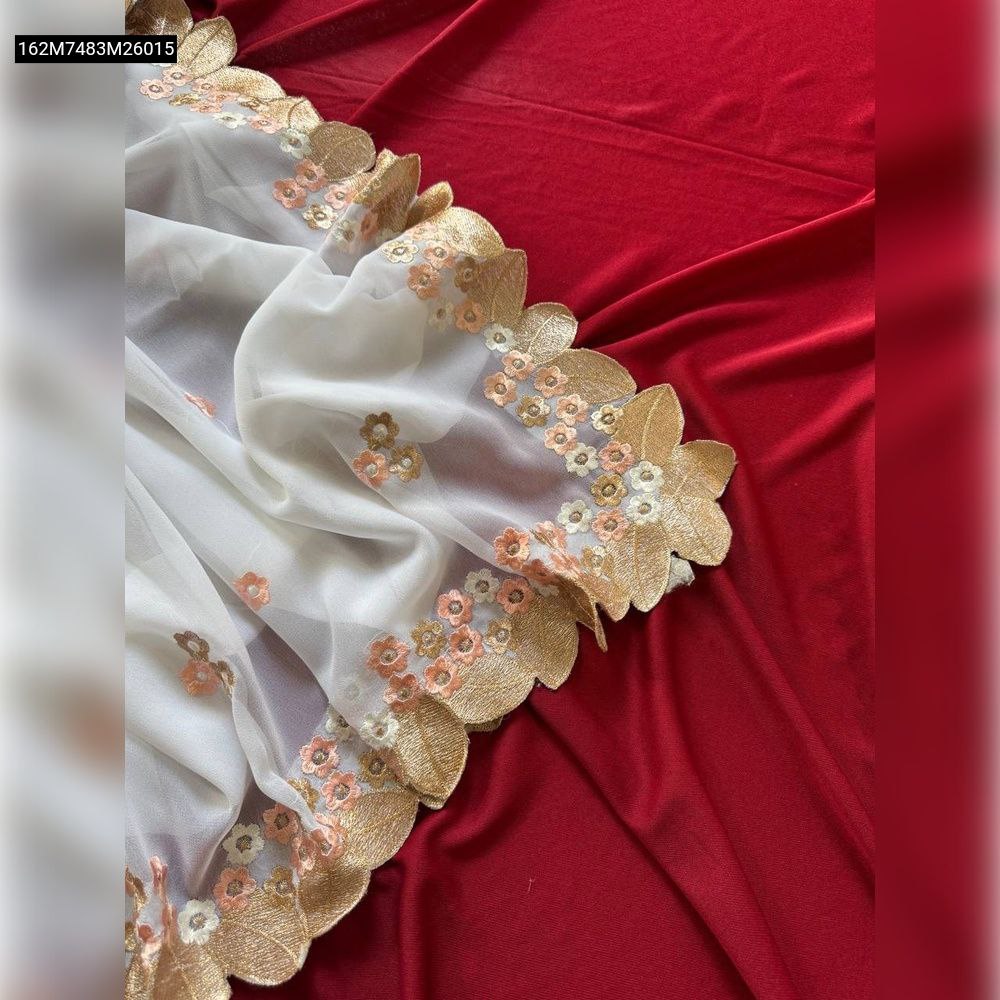 Close-up of TRENDBUY white georgette saree border with peach, gold floral, and golden leaf embroidery on red fabric.