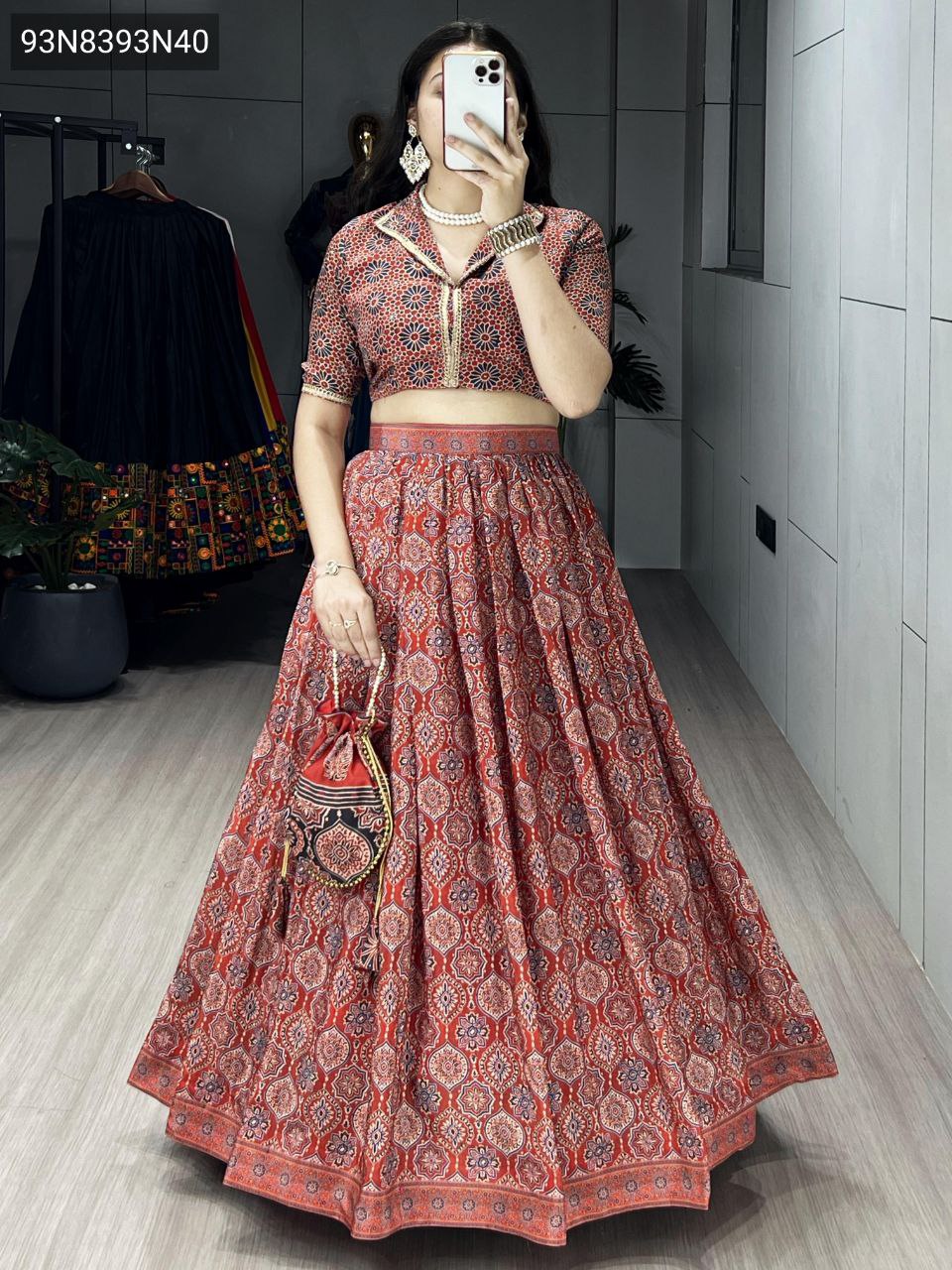 Elegant model showcasing the TRENDBUY Rust Red Azarakh Print Silk Crape Lehenga Choli Set, a full-body shot emphasizing the flared lehenga and coordinated potli bag.