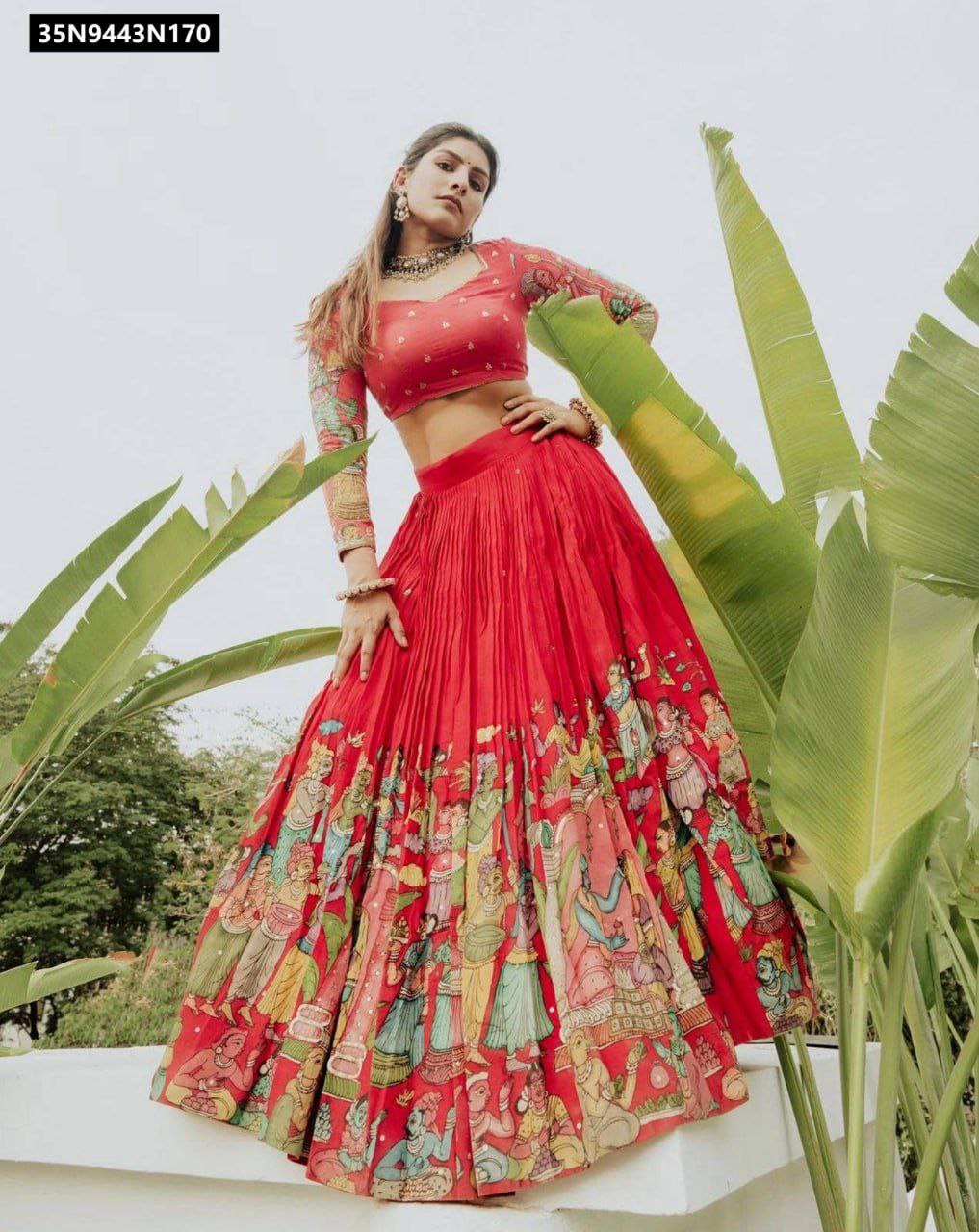 Front view of model wearing TRENDBUY Coral Pink Cotton Kalamkari print lehenga choli with long sleeves, posing elegantly outdoors amidst greenery.