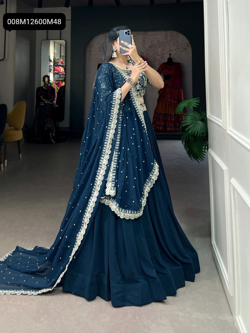 Full shot of a woman in a TRENDBUY Deep Teal Blue Georgette Lehenga Choli with sequin and thread embroidery, capturing a mirror selfie in a stylish boutique.