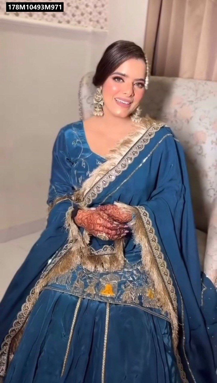 Front portrait of a smiling woman wearing a blue TRENDBUY Lehnga Suit, showcasing intricate gold embroidery and lace details, with mehndi on her hands and traditional jewelry.