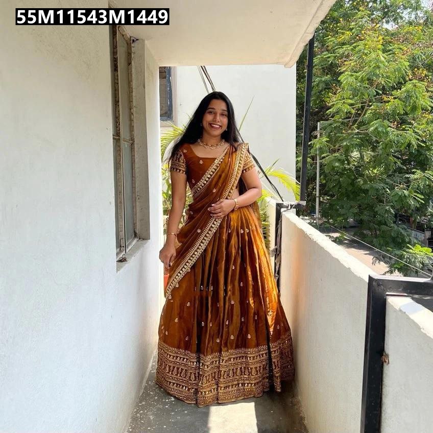 Smiling model showcasing a Golden Bronze TRENDBUY Glass Tissue Silk Half Saree Lehenga with detailed gold embroidery on a balcony with natural light. (Main Image)
