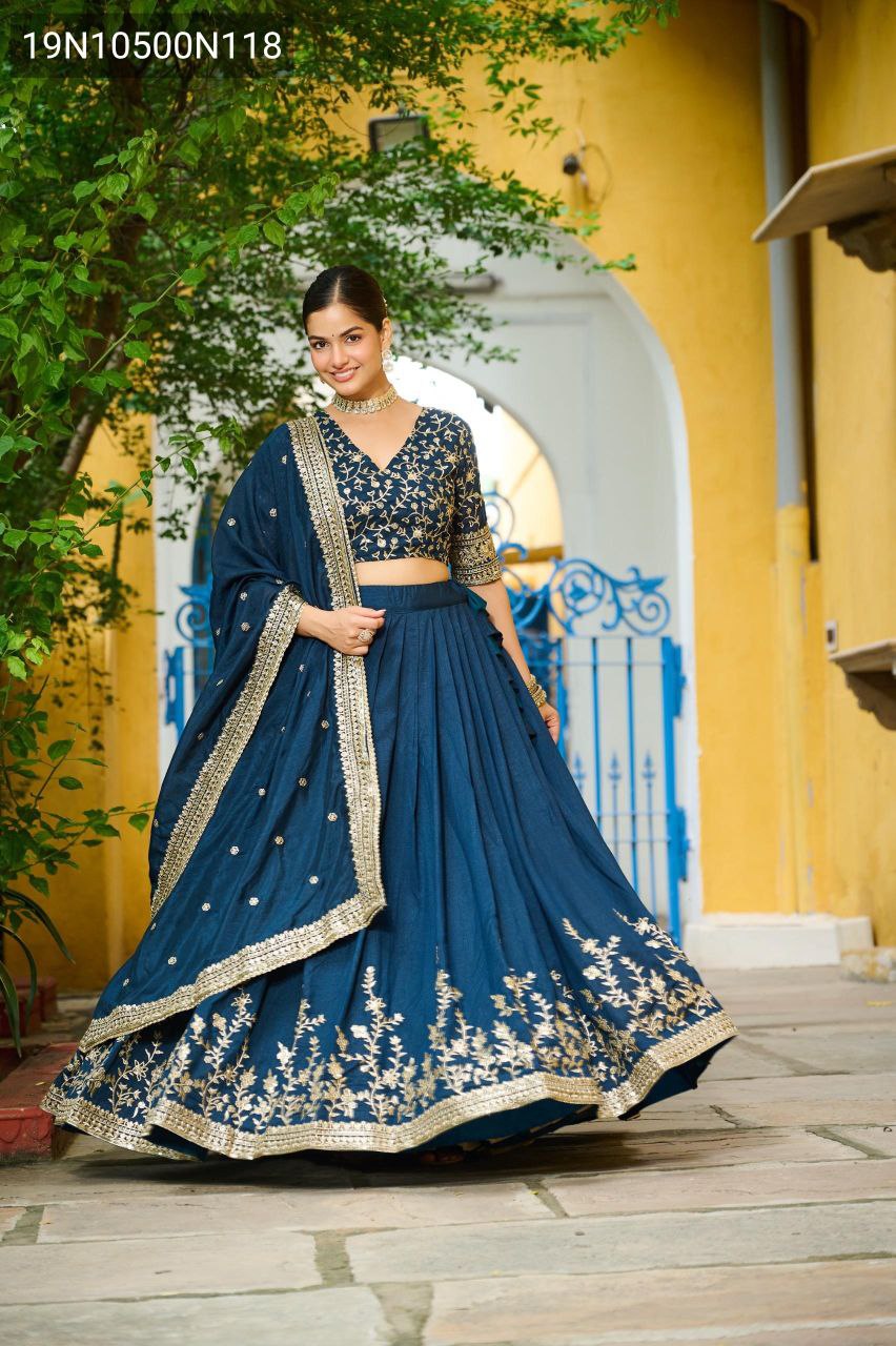 TRENDBUY model in a navy blue Vichitra Silk lehenga choli, featuring gold sequin embroidery, posing gracefully against a yellow wall and blue gate.