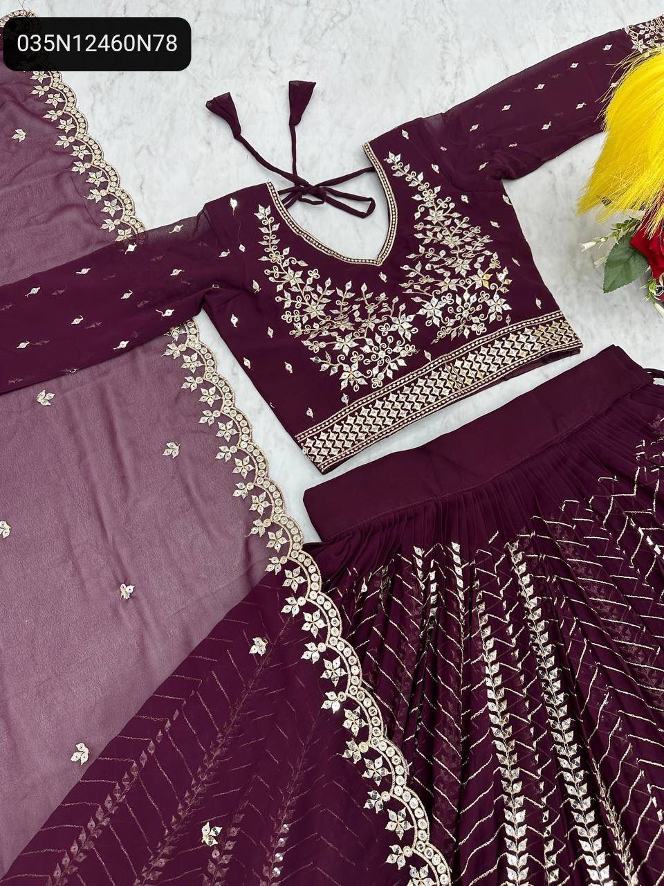 Flat lay of TRENDBUY wine purple georgette lehenga choli and dupatta, showcasing intricate embroidery and sequence work.