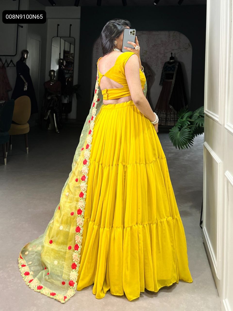 Rear view of a model in a vibrant yellow tiered georgette lehenga with a light green organza dupatta featuring red floral embroidery.