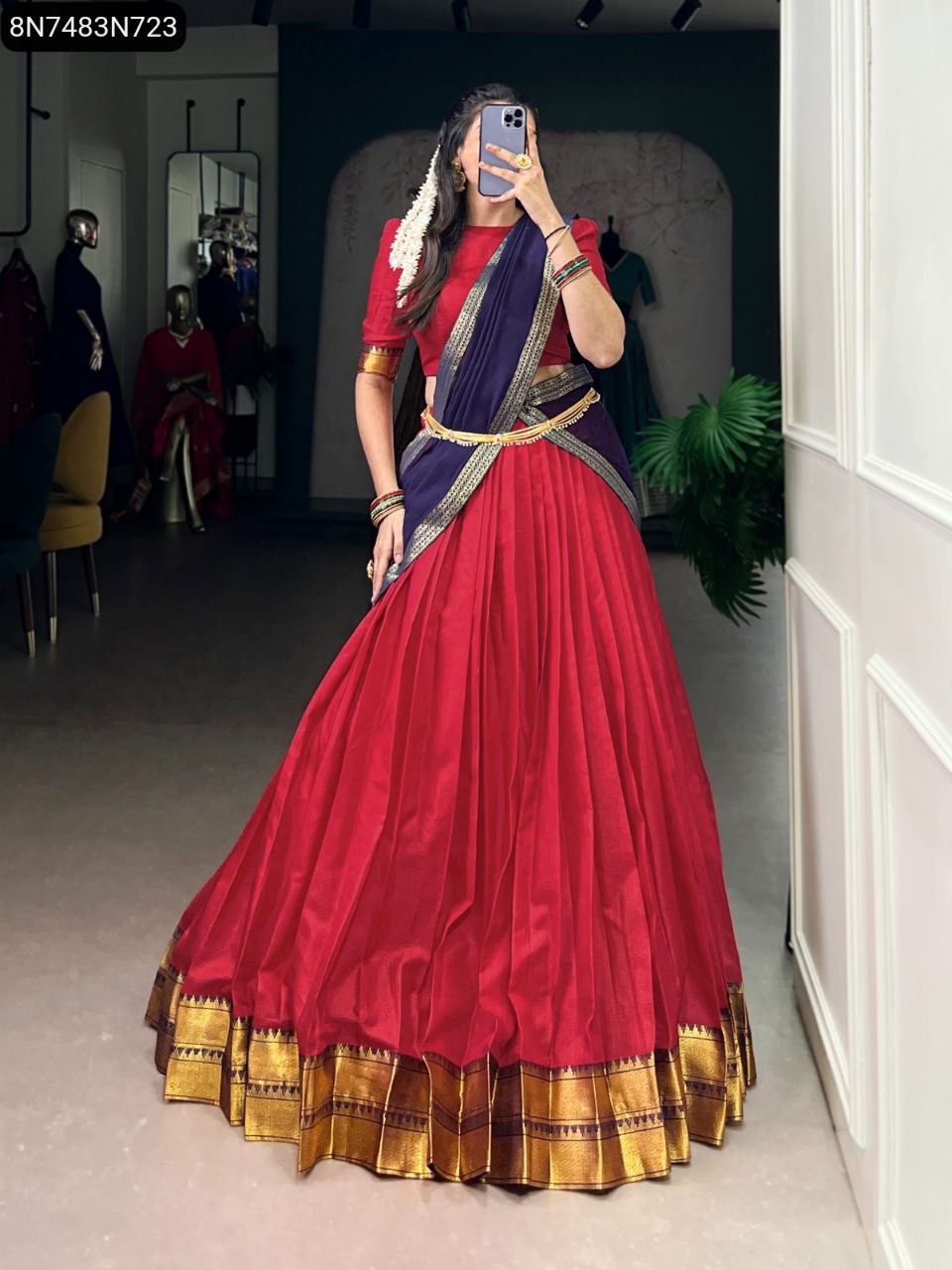 Full shot of model wearing a vibrant red lehenga with a navy blue dupatta, intricate gold zari border, accessorized with a gold waist belt and bangles.