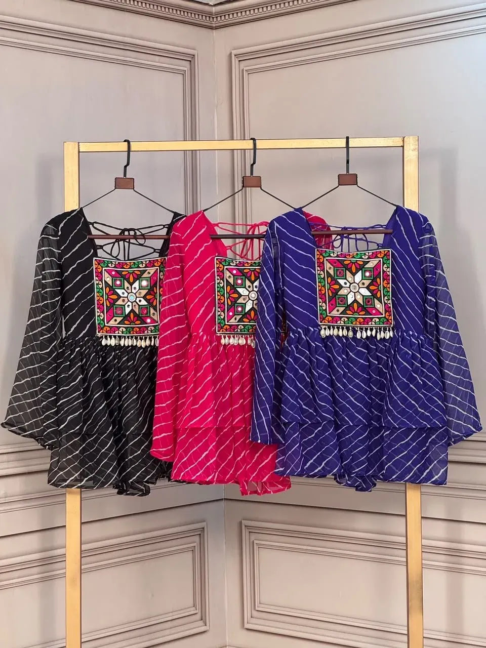 Three Kutchi work tops in black pink and blue hanging on a golden rack