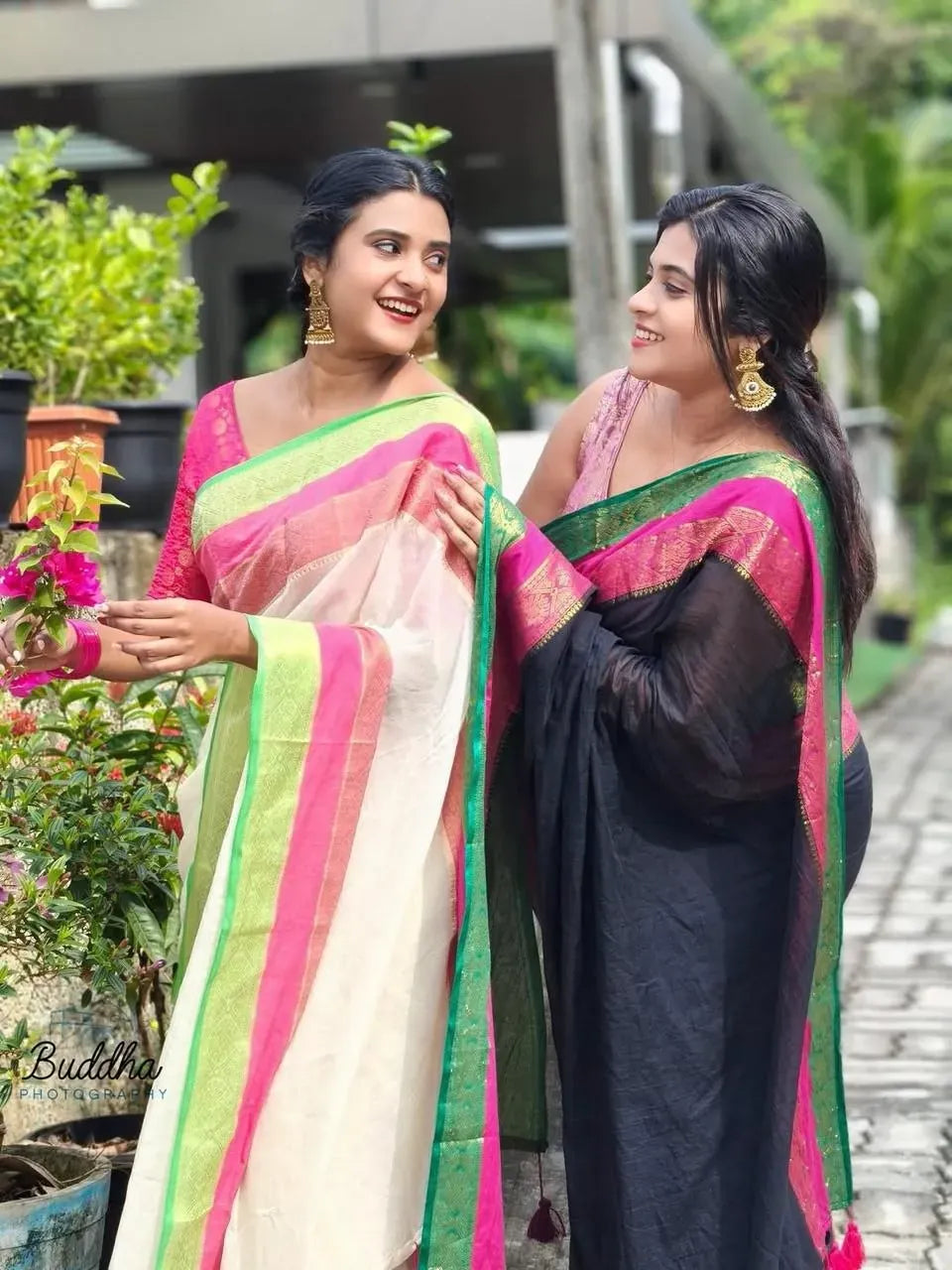 Two women smiling while wearing off-white and black mul cotton sarees