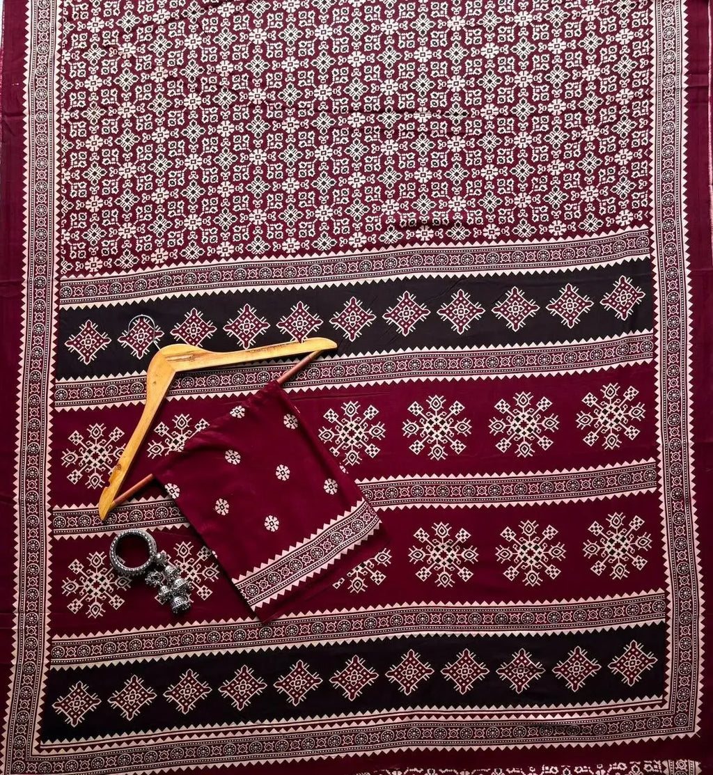 Maroon rayon patola print saree laid flat on surface with wooden hanger and earrings
