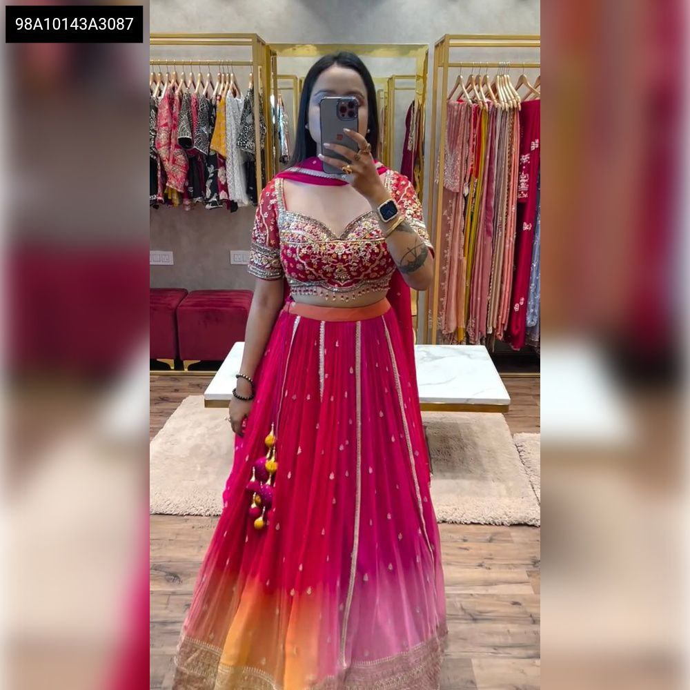 Full body view of a woman wearing a fuchsia ombre Chinon lehenga choli with heavy sequins embroidery, holding a phone for a mirror selfie.