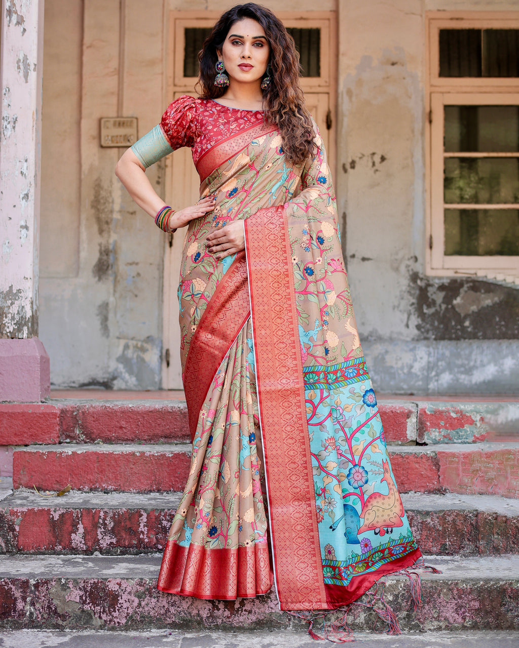 Woman wearing elegant Tussar Silk Saree, beige and aqua with red zari border and floral prints, standing on steps, showcasing ethnic wear.
