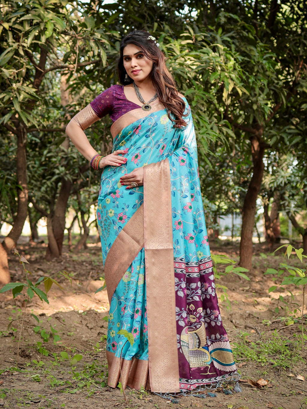 Woman posing elegantly in a TRENDBUY Aqua Blue Tussar Silk Saree with floral prints and a deep wine pallu, showcasing the beautiful drape and gold zari border, set in a natural outdoor background.