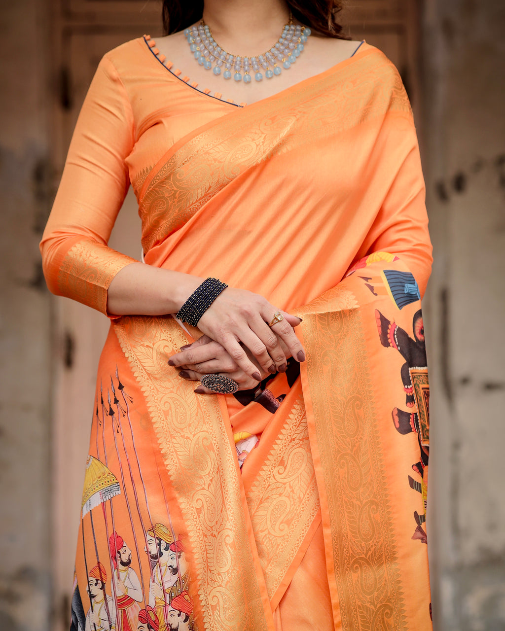 Close-up of the Sunset Orange Tussar Silk Saree showing intricate zari border and Rajasthani procession print.