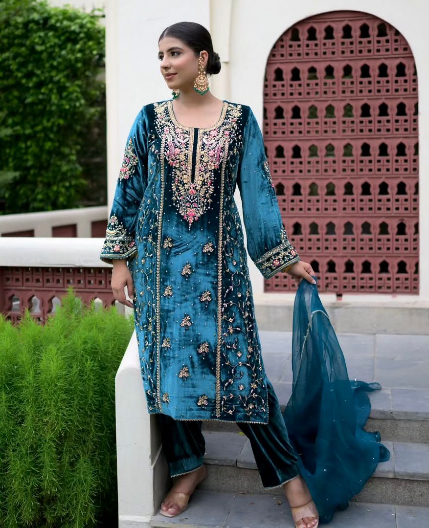 Woman in Teal Green Velvet Embroidered Kurti Set with Palazzo and Organza Dupatta, elegant pose against a traditional wall.
