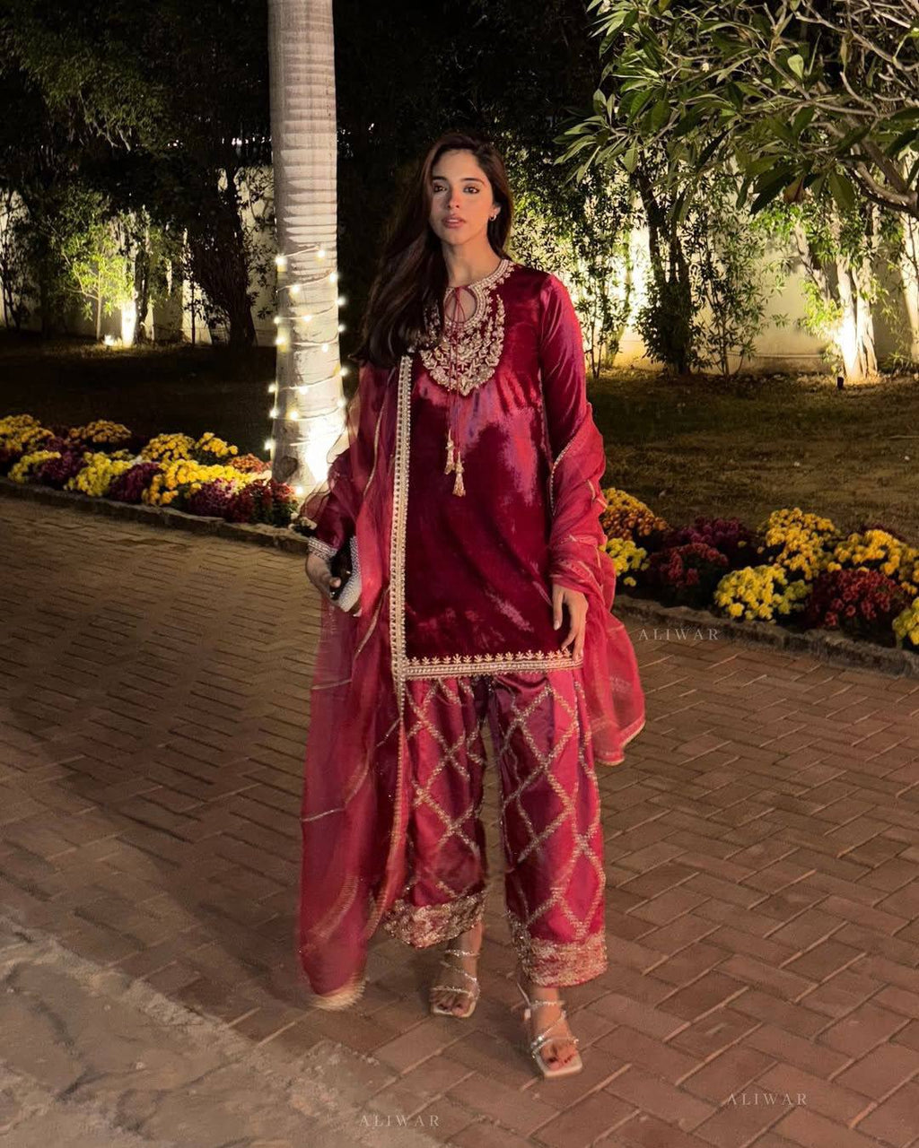 Full body view of a woman posing elegantly in a crimson velvet kurta pant set with intricate embroidery, suitable for festive winter wear.