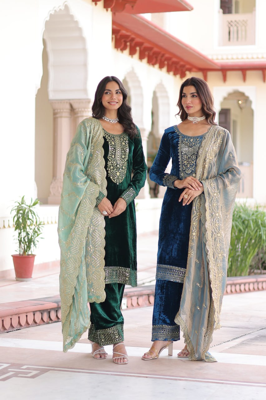 Two women posing in embroidered velvet suits, one deep green, one morpich blue, in an outdoor setting.