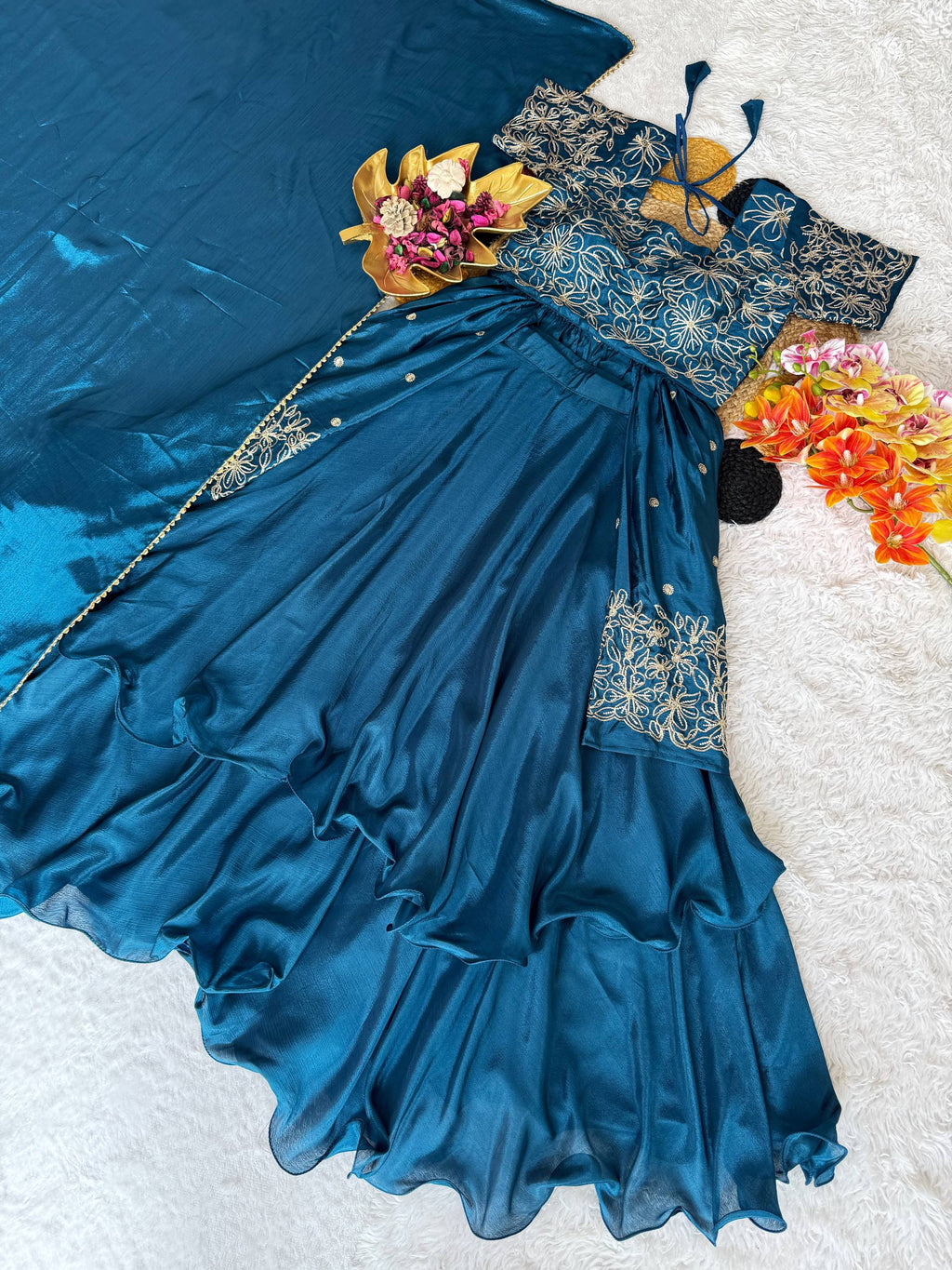 Teal green Chinon silk sequins embroidered lehenga choli set with layered frill detail, displayed on a white textured surface with flowers.