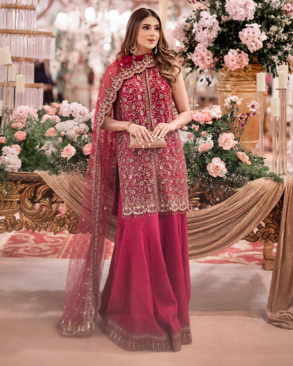 Full body shot of model wearing a fuchsia designer chinnon silk kurta palazzo set with gold embroidery, posing elegantly in a festive setting.