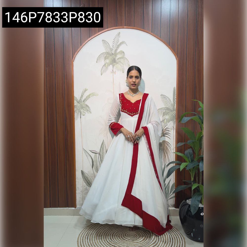 Full shot of model wearing white and red Indo-Western gown with handwork embroidery, standing against a patterned wall.