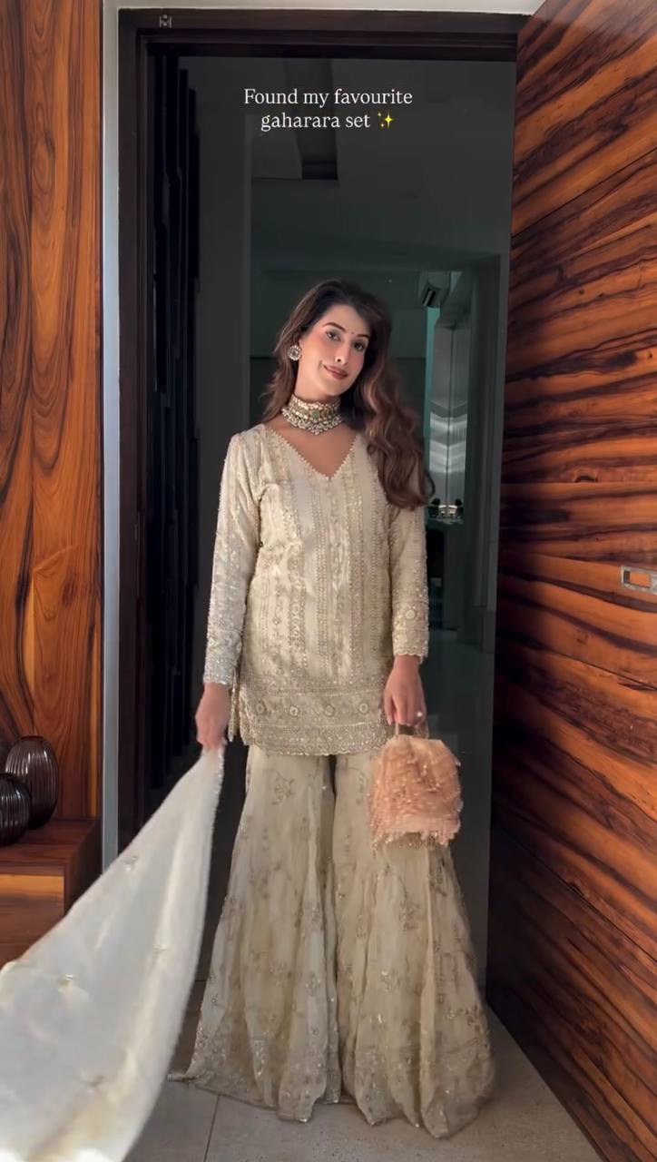 Full body shot of a woman in an embroidered creamy beige faux georgette palazzo suit set with dupatta.
