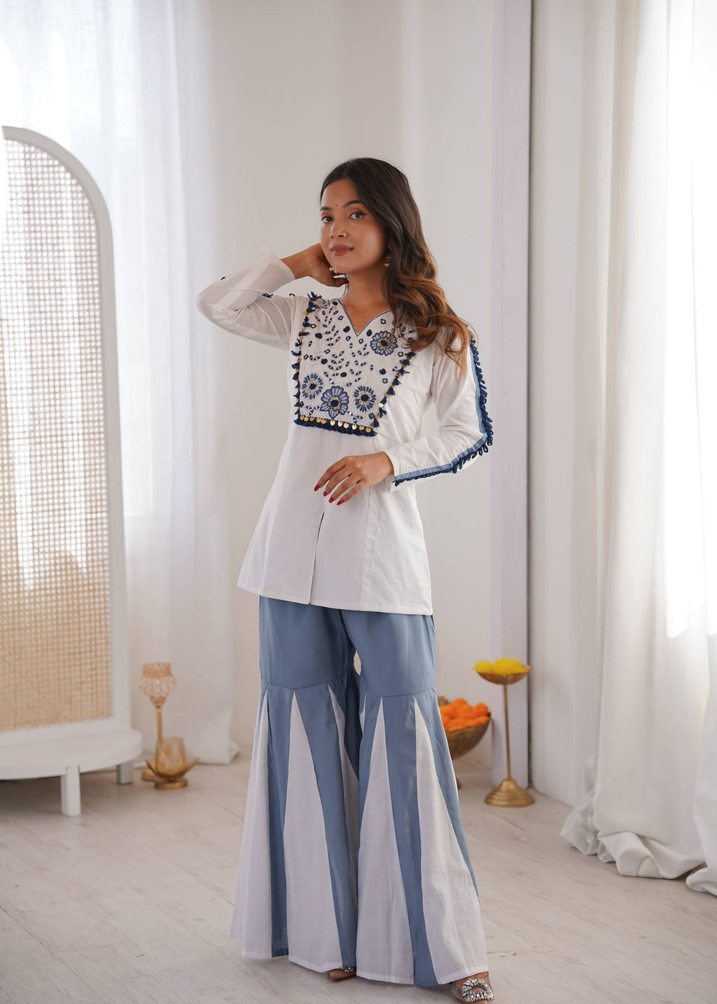 Woman posing in white and blue Roman Silk embroidered co-ord set with mirror work, front-facing.