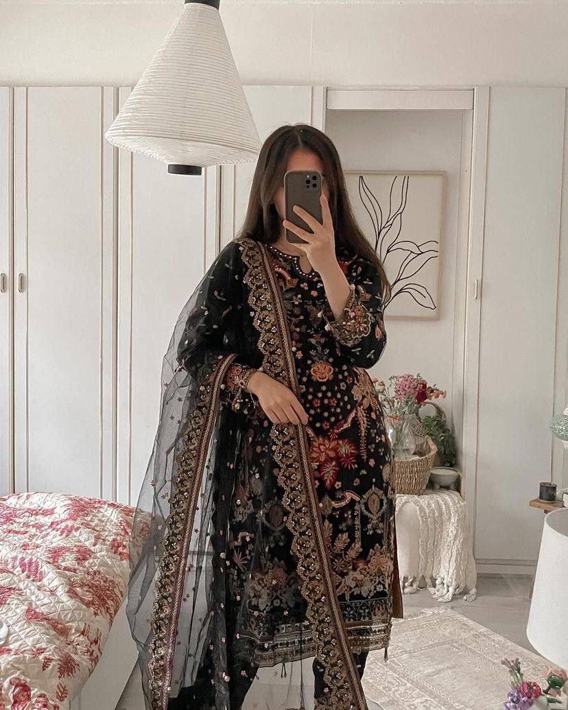 Woman wearing a black heavy sequence embroidered faux georgette suit set with a matching net dupatta, full view.