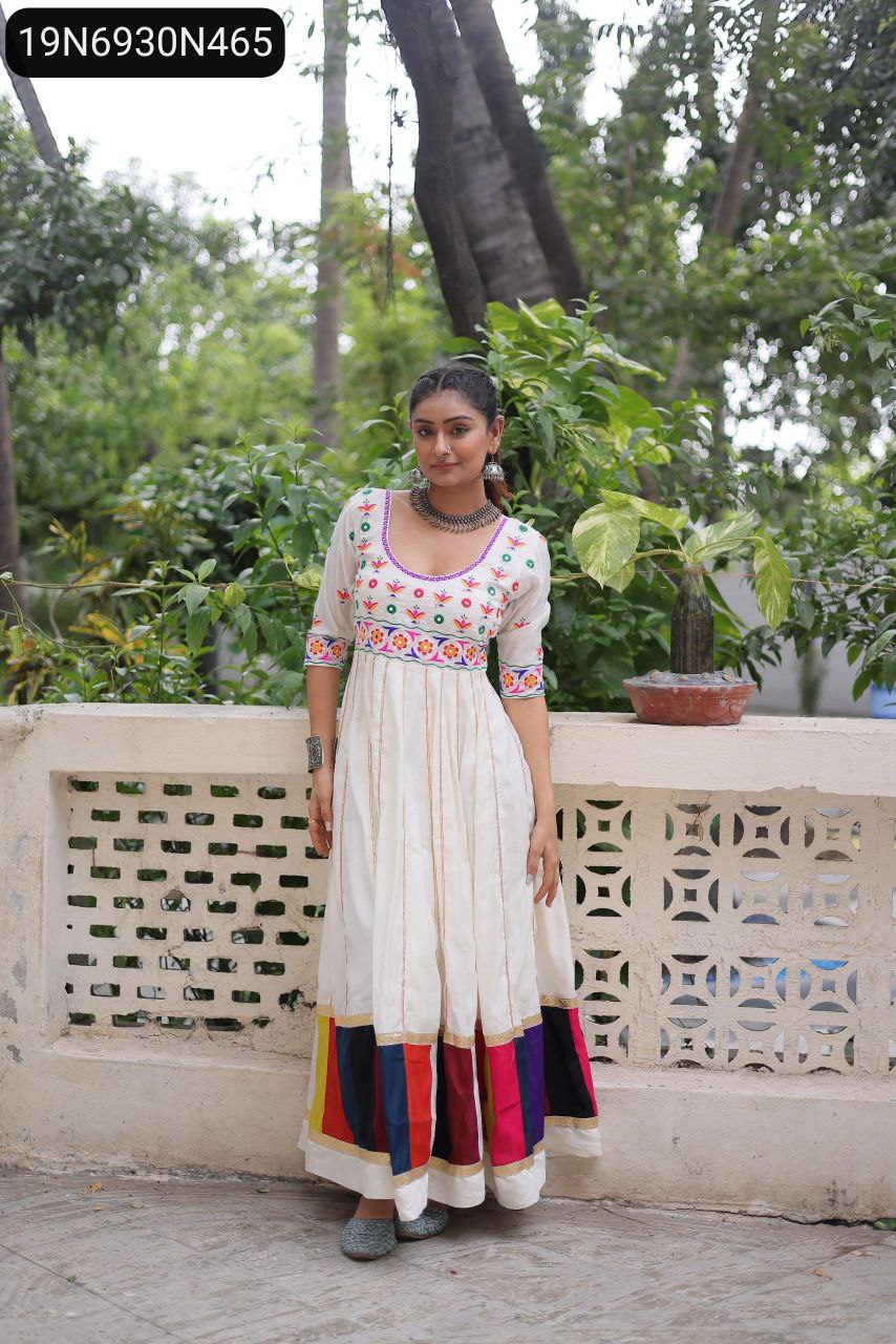 Woman posing in a white Roman gown with multicolour thread work and a vibrant border, outdoors.