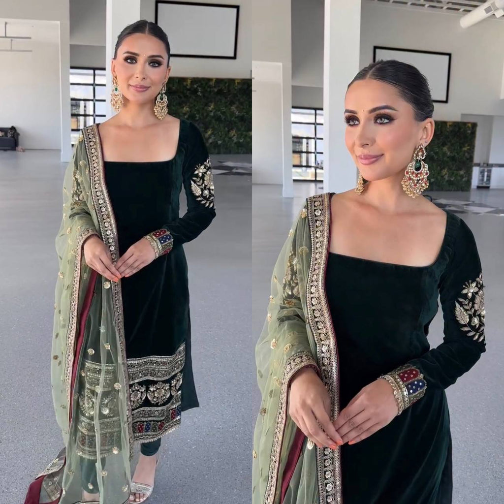 Model posing in an Emerald Green Viscose Velvet Suit Set with intricate gold and colorful embroidery, paired with a sheer, sequined light green dupatta.
