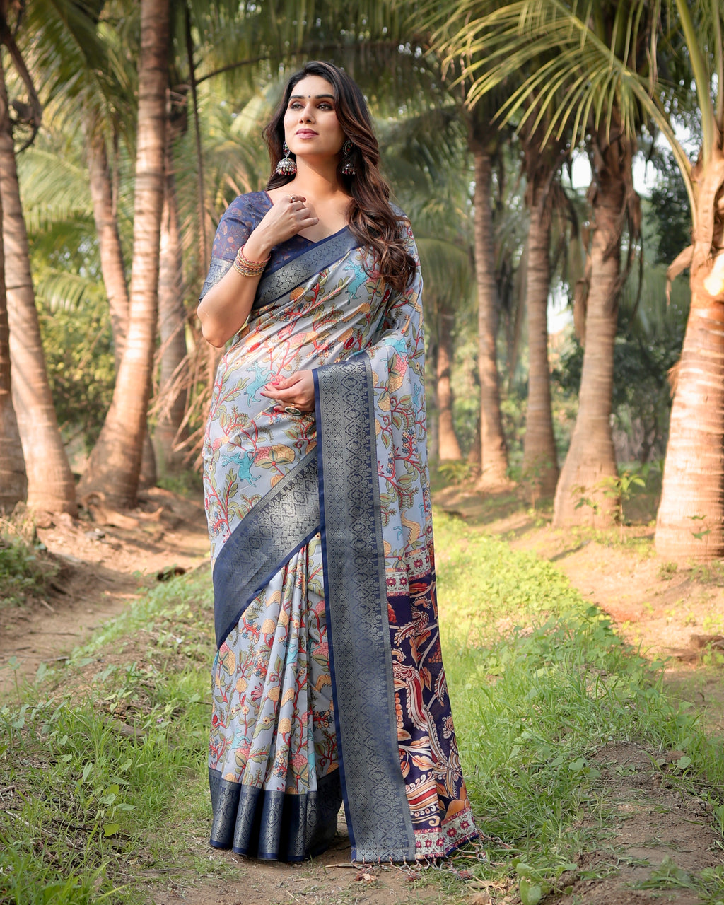 Elegant woman in a sky blue Tussar silk saree with floral paisley design posing gracefully amidst nature.