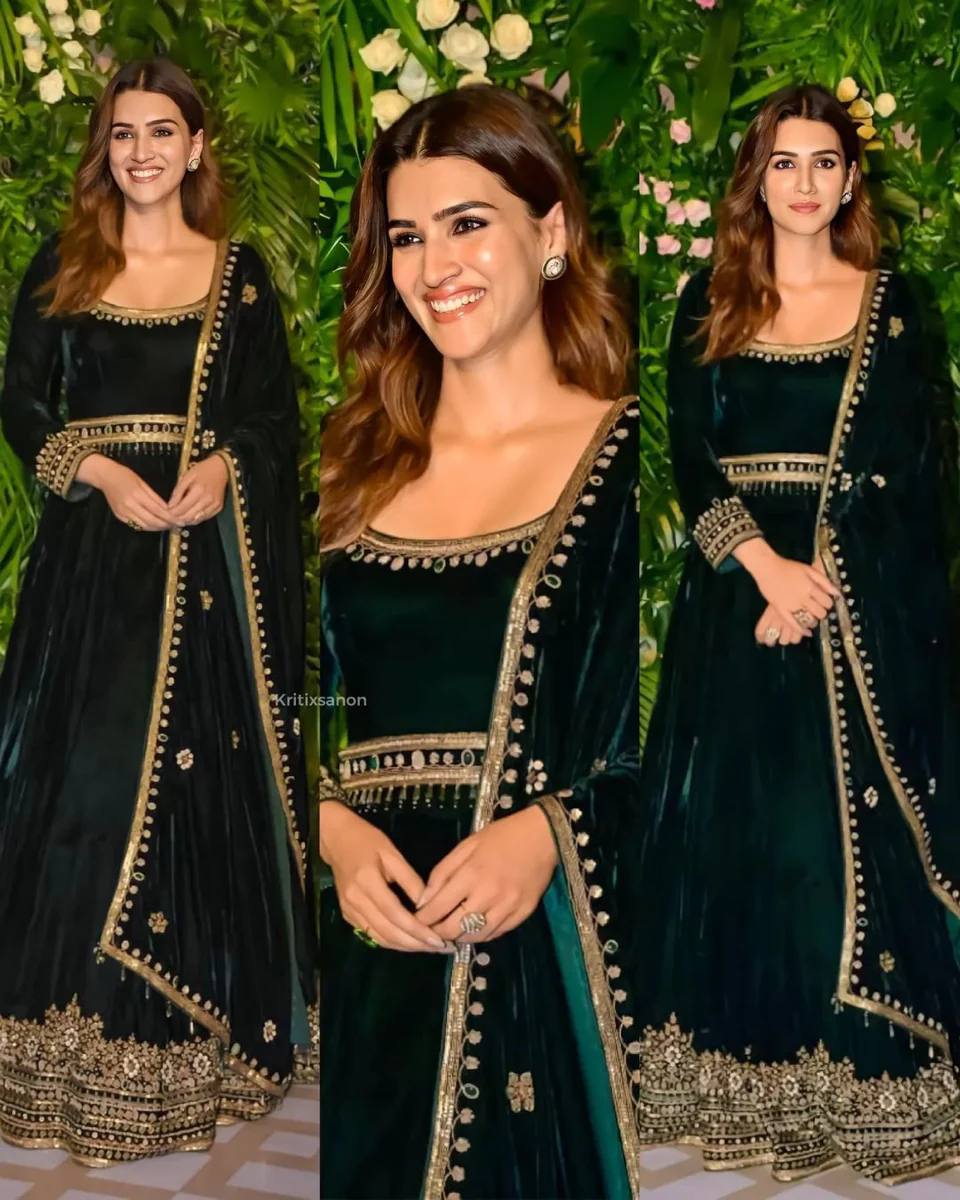 Elegant woman in a deep green velvet anarkali gown with golden embroidery and matching dupatta, smiling at a party.