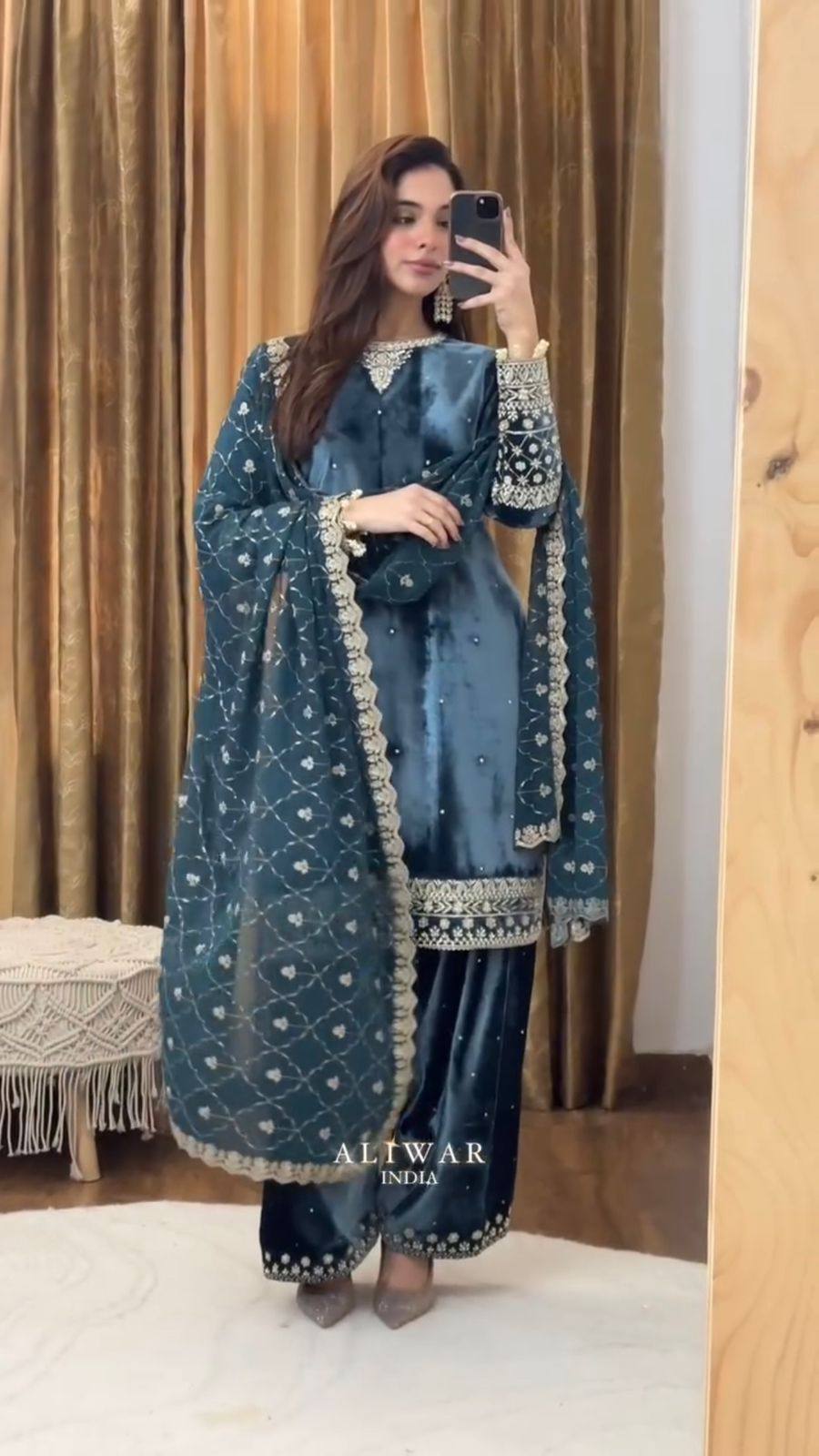 Front view of a woman posing in a luxurious teal blue velvet embroidered kurta pant set with georgette dupatta.