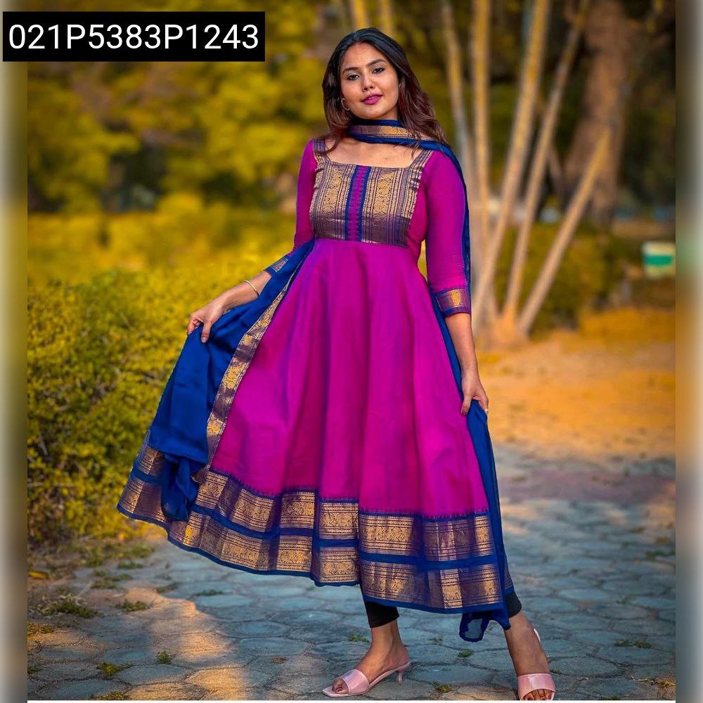 Full body shot of a woman posing in a vibrant magenta Anarkali gown with royal blue dupatta and gold zari border, in a park setting.